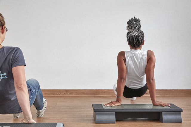 Eine krebserkrankte junge Frau, die gemeinsam mit einem Sporttherapeut, anstrengendere Körpergewichtsübungen durchführt